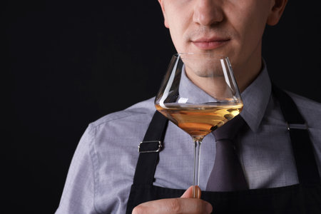 Professional sommelier tasting white wine on black background