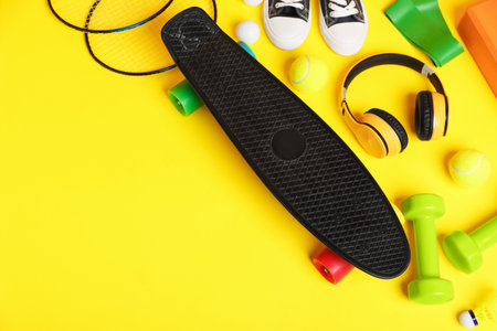 Penny board, sneakers, headphones and sports equipment on yellow background, flat lay. Space for textの写真素材