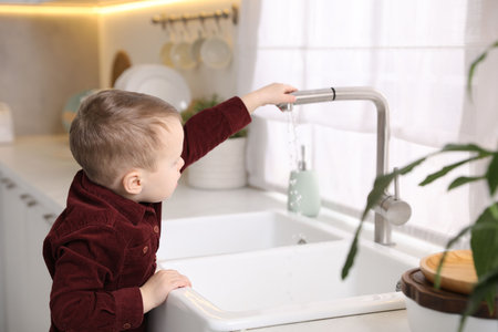Child safety at home. Little boy opening faucet at sink in kitchenの写真素材