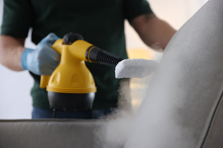 Pest control worker cleaning cushion with steam cleaner indoors, closeupの写真素材