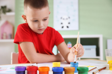 Cute little boy painting with brush at table indoors, selective focusの写真素材
