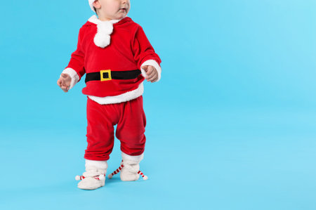Cute child in Santa costume on light blue background. Baby's first Christmasの写真素材