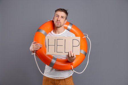 Unhappy man with lifebuoy and cardboard sign with word Help on grey background