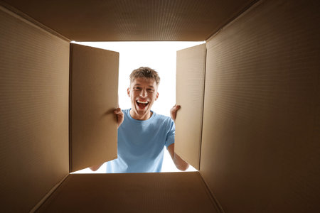 Man looking into cardboard box against white background, view from inside package