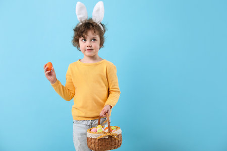 Easter celebration. Cute little boy in headband with bunny ears and wicker basket full of painted...