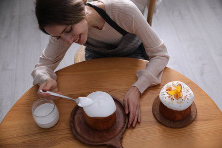 Young woman decorating traditional Easter cake with glaze at wooden table, above view