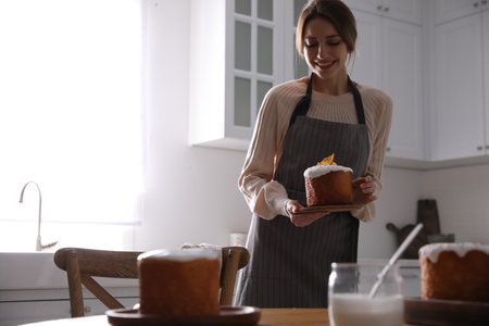 Young woman with traditional decorated Easter cake in kitchen, space for text
