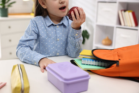 Girl with apple packing her backpack for school at desk indoors, closeup
