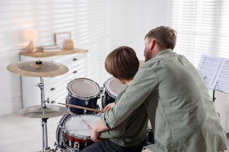 Little boy learning how to play drums with music teacher indoors, back view