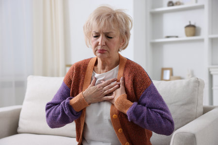 Heart attack. Senior woman suffering from pain in chest indoors