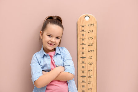 Little girl measuring her height with chart near beige wallの写真素材