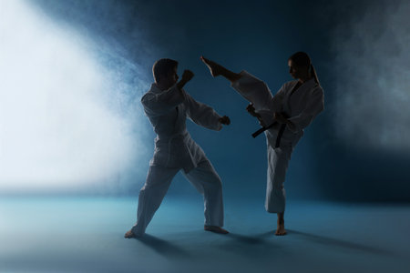 Man and woman in uniforms practicing karate on dark blue background