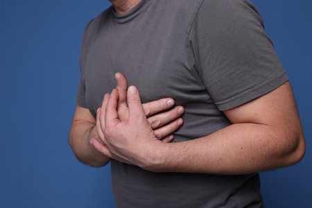Heart attack. Man suffering from pain in chest on blue background, closeup