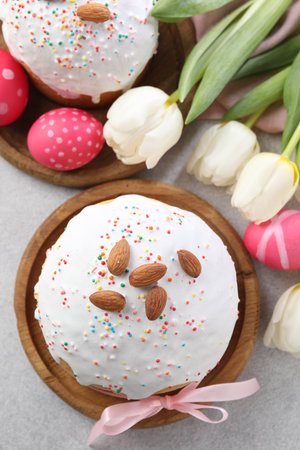 Tasty Easter cake, painted eggs and tulips on light gray table, flat lay