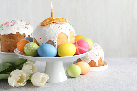 Tasty Easter cakes, painted eggs and tulips on light gray table, space for text