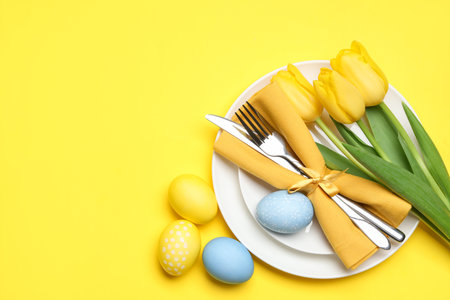 Easter celebration. Festive table setting with tulip flowers and painted eggs on yellow background,...