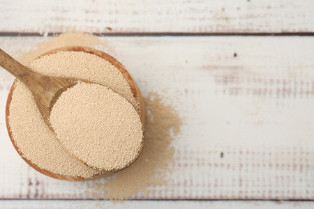 Dry yeast in bowl and spoon on white wooden table, top view. Space for textの写真素材