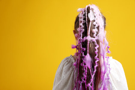 Girl with stylish hairstyle on yellow background, back view. Space for text
