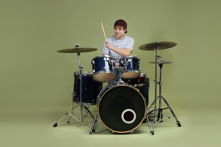 Smiling teenage boy in baseball cap with drumsticks learning how to play drums on green backgroundの写真素材