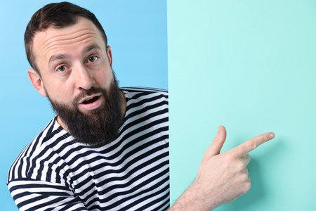 Surprised man with mustache and beard pointing at poster on light blue background. Space for textの写真素材