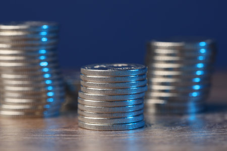 Stacked coins on wooden table against blue background, closeupの写真素材