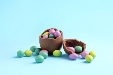 Broken chocolate egg with colorful candies on light blue background. Happy Easterの写真素材
