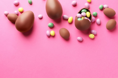 Chocolate Easter eggs with candies on pink background, flat lay. Space for text