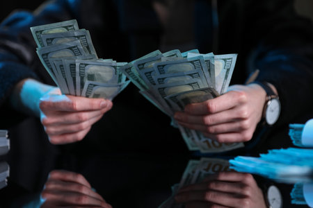 Young businessman with dollar banknotes at mirror table in dark room, closeupの写真素材