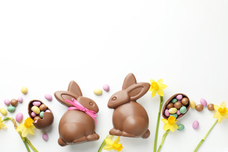 Chocolate Easter bunnies, flowers, ribbon and eggs on white background, flat lay. Space for text