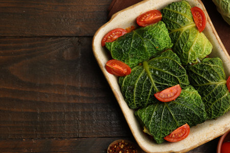 Stuffed cabbage rolls in baking dish and ingredients on wooden table, top view. Space for text