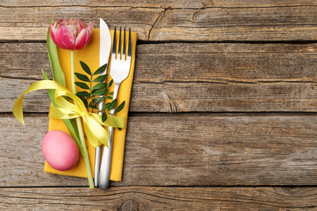 Easter table setting. Beautiful silverware with tulip and painted egg on wooden background, top...