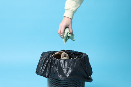 Woman throwing napkin into trash bin on light blue background, closeupの写真素材