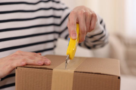 Woman opening parcel with knife at home, closeup