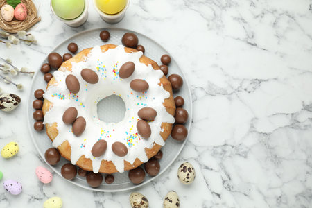 Delicious Easter cake, chocolate candies, willow branches, quail and painted eggs on white marble...