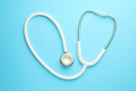 White stethoscope on light blue background, top view