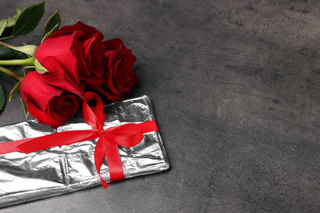 Beautiful roses and wrapped gift on gray background, closeup. Space for textの写真素材
