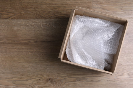 Bubble wrap in cardboard box on wooden table, top view. Space for text