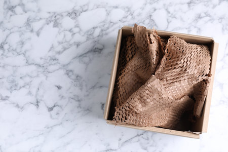 Cardboard box with honeycomb kraft paper on white marble table, top view. Space for text