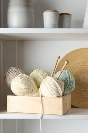 Knitting yarns and needles in crate on shelf indoors