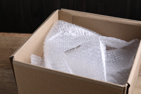 Bubble wrap in cardboard box on wooden table, closeup