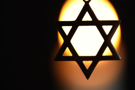Holocaust Remembrance Day. Pendant in shape of Star of David against black background with blurred light, closeup. Space for textの写真素材