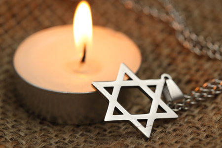 Holocaust Remembrance Day. Pendant in shape of Star of David and burning candle on burlap cloth,...