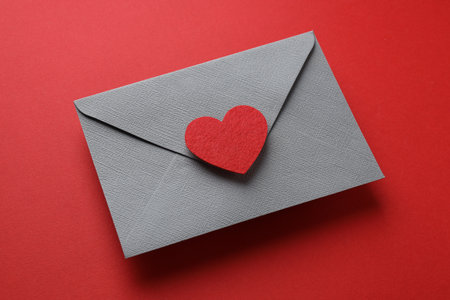 Happy Valentine's day. Envelope with greeting card and decorative heart on red background, closeup