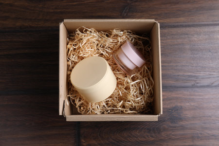 Shredded paper filling and jars of cream in cardboard box on wooden tableの写真素材
