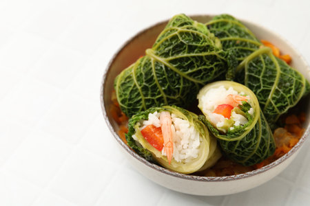 Stuffed cabbage rolls with vegetables on white tiled table, closeup. Space for text