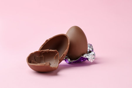Whole and broken chocolate eggs on pink background. Happy Easter