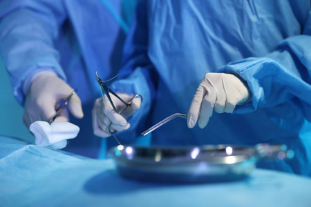 Professional surgeons with medical instruments performing operation in surgery room, closeup