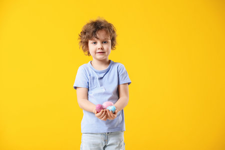 Easter celebration. Portrait of cute little boy holding painted eggs on yellow background, space for...