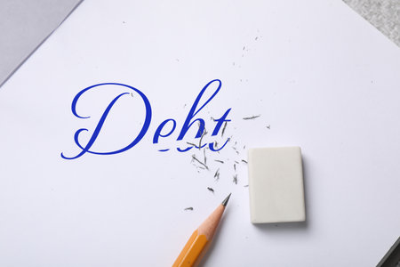 Erasing word Debt written in notebook on table, top view