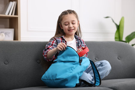Girl packing her backpack for school on sofa at home
